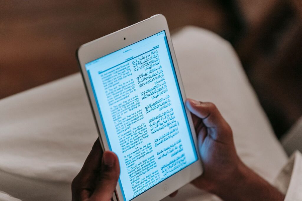 Crop unrecognizable person in casual clothes reading text on tablet against blurred background in room